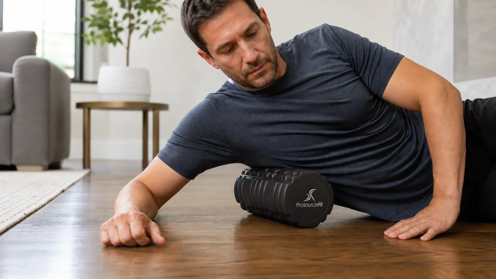 Foam roller positioned under a person's calves as they sit on the floor with hands behind them for support