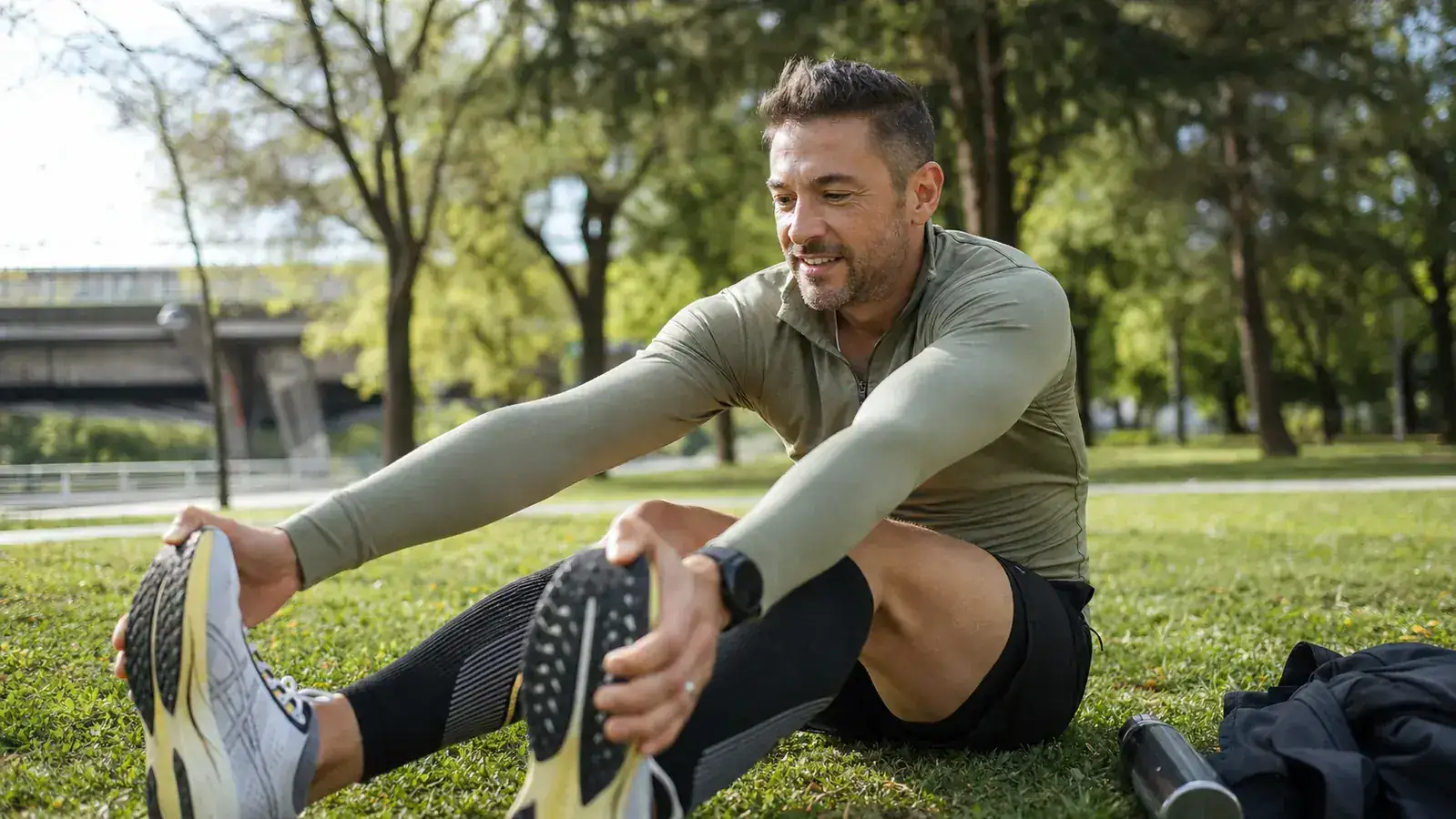 Runner stretching calves against a park bench post-run, compression sleeves visible