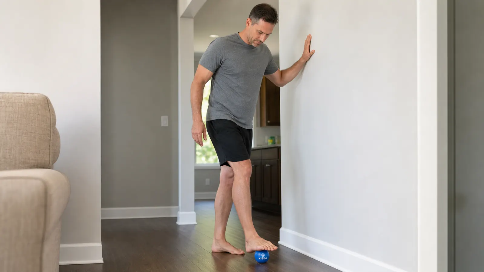 Man standing on a lacrosse ball with one hand on a wall for balance, demonstrating weight-bearing pressure technique