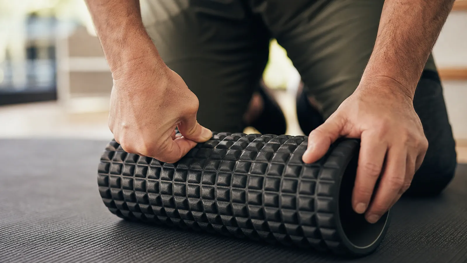Trail runner sitting on a gym floor using a foam roller on his IT band after a run