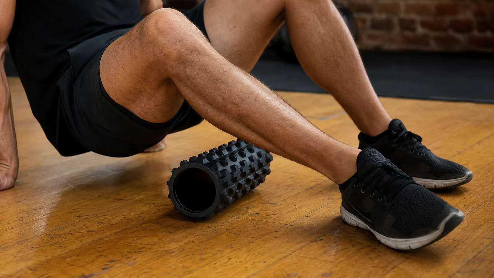 Man sitting on a trail after a run using the massage gun on his calf, trees in background